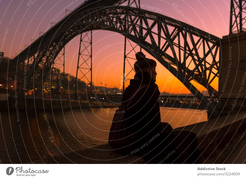 Frau sitzt bei Sonnenuntergang auf der Böschung Tourist Stauanlage Großstadt Brücke Fluss sitzen Borte Wasser Architektur Wahrzeichen Himmel wolkenlos Abend