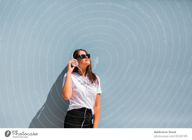 Fröhliche, ungezwungene Frau mit Sonnenbrille steht auf Stadtstraße Kopfhörer stylisch heiter trendy tausendjährig schön Apparatur Musik Gerät stehen Generation