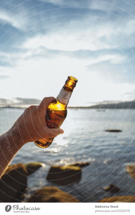 Bierflasche in der Hand mit Meereslandschaft im Hintergrund MEER Küste Sonnenlicht Flasche jubelt Seeküste Alkohol Strand durch Erfrischung Party reisen trinken