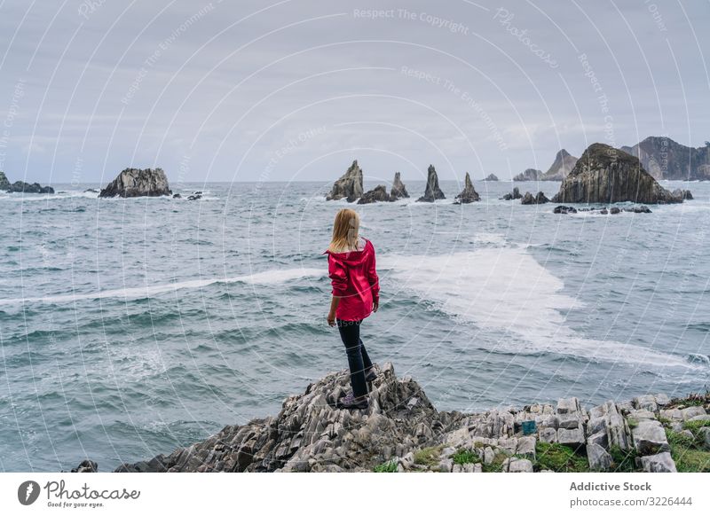 Frau an steiniger Meeresküste mit Blick auf schäumendes Wasser, das die Spitzen des Wassers spült zuschauend Urlaub Tourismus Feiertag entspannend Abenteuer