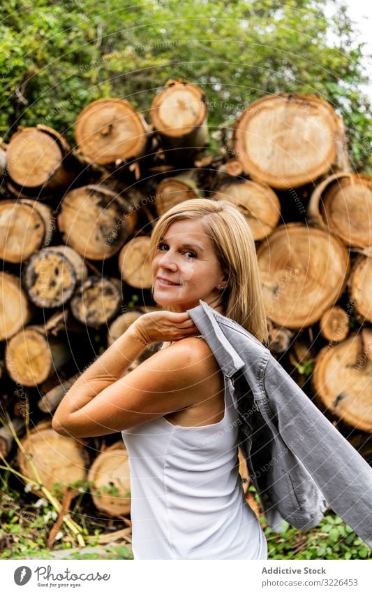 Frau zieht Jacke vor dem Hintergrund eines Holzstapels im Wald aus Totholz laufen Kofferraum Brennholz Gesicht Model Natur Feiertag Lächeln Urlaub Wetter Dame