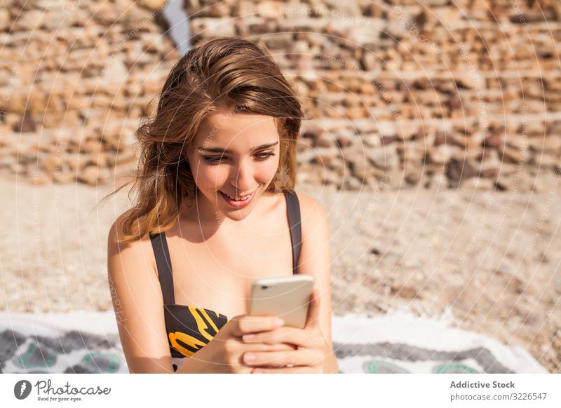 Frau im Badeanzug mit Mobiltelefon am Strand MEER Smartphone Urlaub hübsch heiter modisch Glück stylisch trendy Badebekleidung sitzen genießen