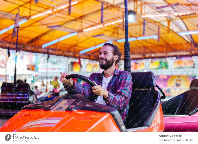 Glücklicher Hipster-Mann fährt Elektroauto im Vergnügungspark Mitfahrgelegenheit Vergnügen Park freudig lässig Lächeln Spaß haben Anziehungskraft Karneval