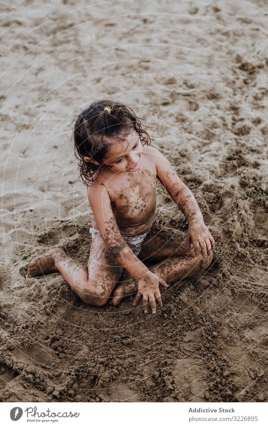 Inspiriertes Kind spielt mit Sand am Strand spielen Sommer Urlaub beschmiert Schürfen Feiertag Spaß Spielen Mund Mädchen Genuss Ausdruck Aktivität heiter