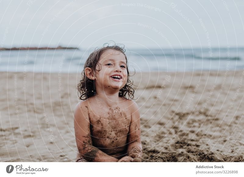 Inspiriertes Kind spielt mit Sand am Strand spielen Sommer Urlaub beschmiert Schürfen Feiertag Spaß Spielen Mund Mädchen Genuss Ausdruck Aktivität heiter