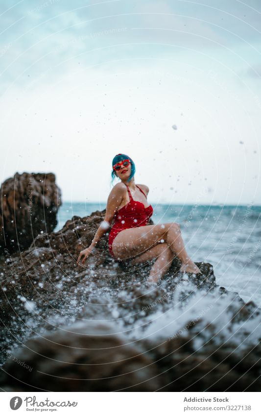 Anmutige Frau mit trendiger Frisur bräunt sich auf felsigem Stein im Wasser stylisch MEER Ufer retro Erholung Mode altehrwürdig elegant Genuss Badebekleidung