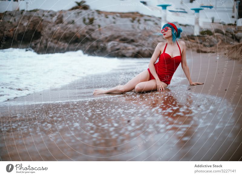 Entspannte Frau im hellen stilvollen Badeanzug am Sandstrand sitzend Strand stylisch MEER retro Sitzen Erwachsener sandig sinnlich Erholung Mode altehrwürdig