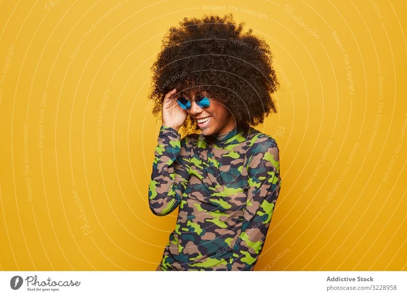 Trendige ethnische Dame mit Sonnenbrille vor hellem Hintergrund Frau farbenfroh cool Afro-Look trendy pulsierend Glück lebhaft Outfit modern Hipster