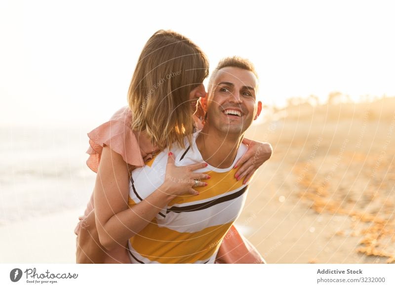 Mann trägt Frau auf dem Rücken in Meeresnähe Paar Strand Resort Liebe MEER Huckepack Mitfahrgelegenheit Lächeln Glück Urlaub Spaß winken Wasser Erwachsener