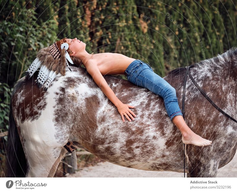 Friedliche Tagträume eines Kindes im Liegen auf einem Pferd Junge Harmonie authentisch Lügen Kriegsmütze Pferderücken Liebe Art Inder Tracht Wachtraum