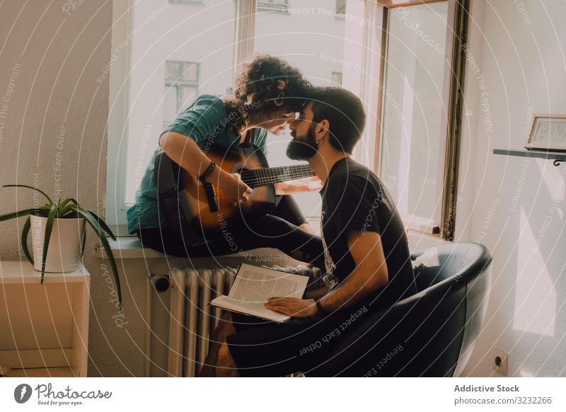 Fröhliches Paar verbringt Zeit miteinander zu Hause heimwärts Gitarre Küssen spielen Zusammensein Buch lesen Glück heiter Lächeln zuhören Hobby Zeitvertreib