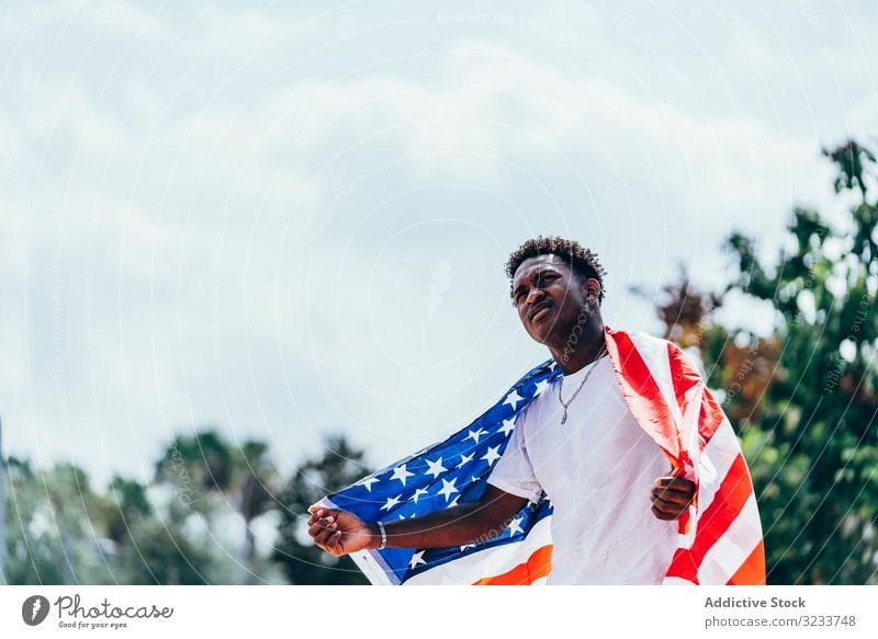 Schwarzer Mann wickelt sich draußen in amerikanische Flagge ein Amerikaner Fahne eingewickelt schwarz Afroamerikaner national Selbstständigkeit aktiv 4. Juli