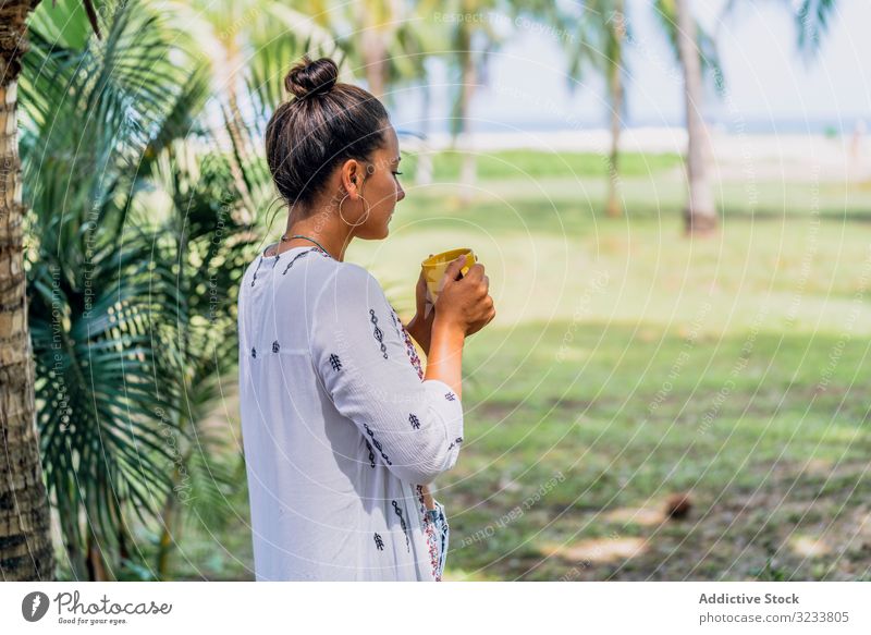 Entspannte Frau genießt heißes Getränk und steht auf exotischem Rasen entspannt Heißgetränk Seeküste Palme sonnig trinken friedlich Kaffee Becher stehen Gras