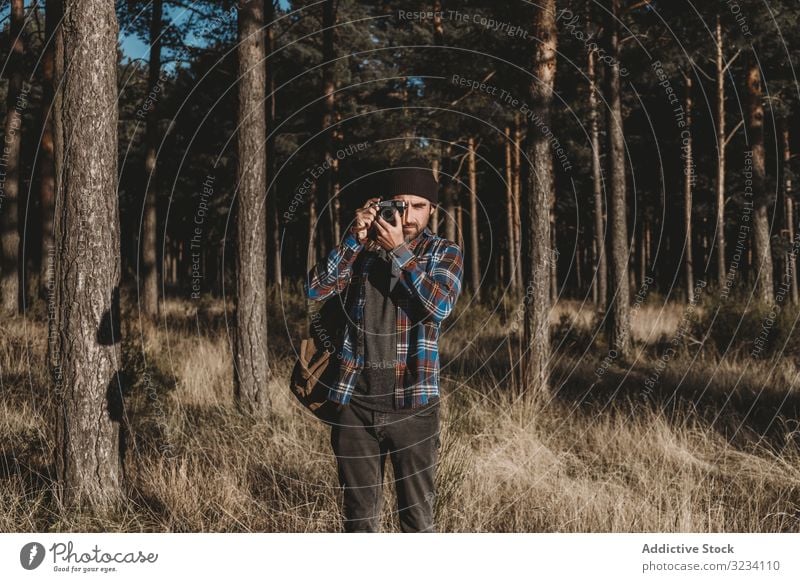 Zuversichtlicher Fotograf fotografiert mit der Kamera im sonnigen Wald Fotografie Fotokamera selbstbewusst fotografierend Immergrün Baum Gras getrocknet Herbst