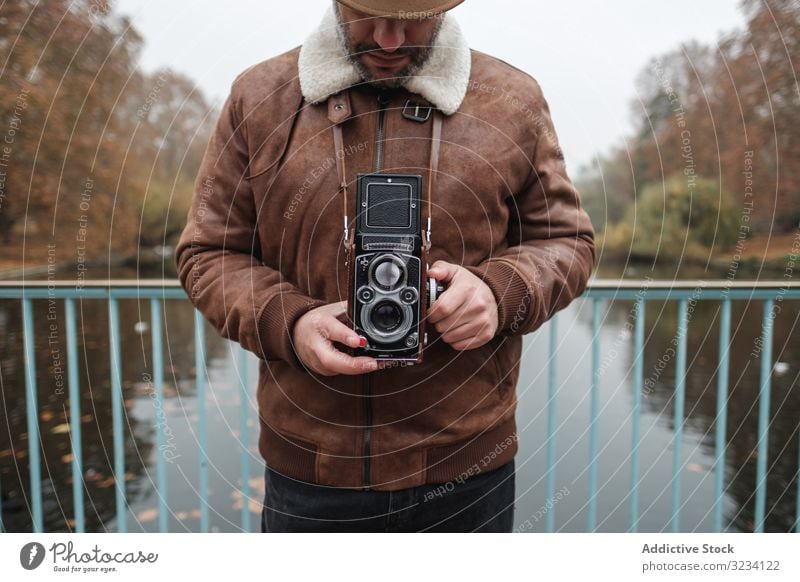 Männlicher Tourist mit altertümlicher Kamera am Fluss Brühe Fotoapparat Park Brücke Mann Herbst Windstille London Großbritannien reisen Wasser retro