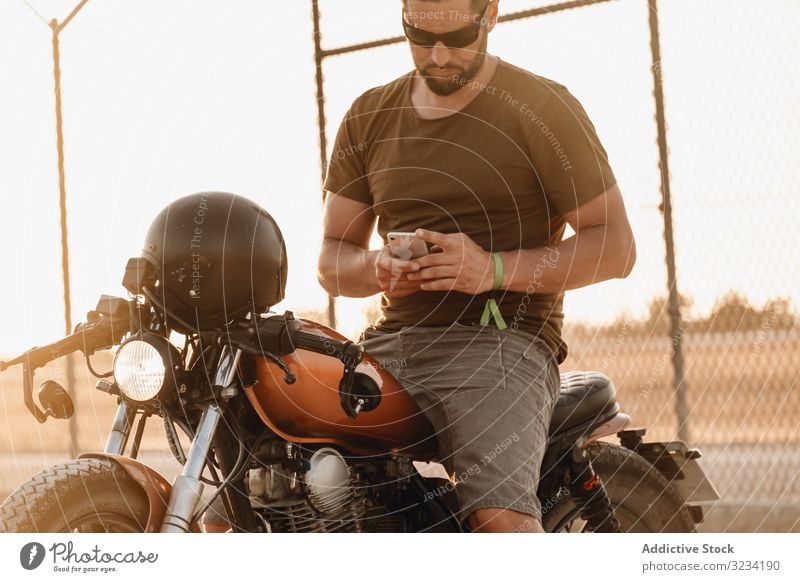 Mann sitzt auf Motorrad und surft mobil Smartphone moto ruhen benutzend Surfen Sonnenbrille fokussiert wehmütig sitzen Mobile männlich Feld Verkehr Straße
