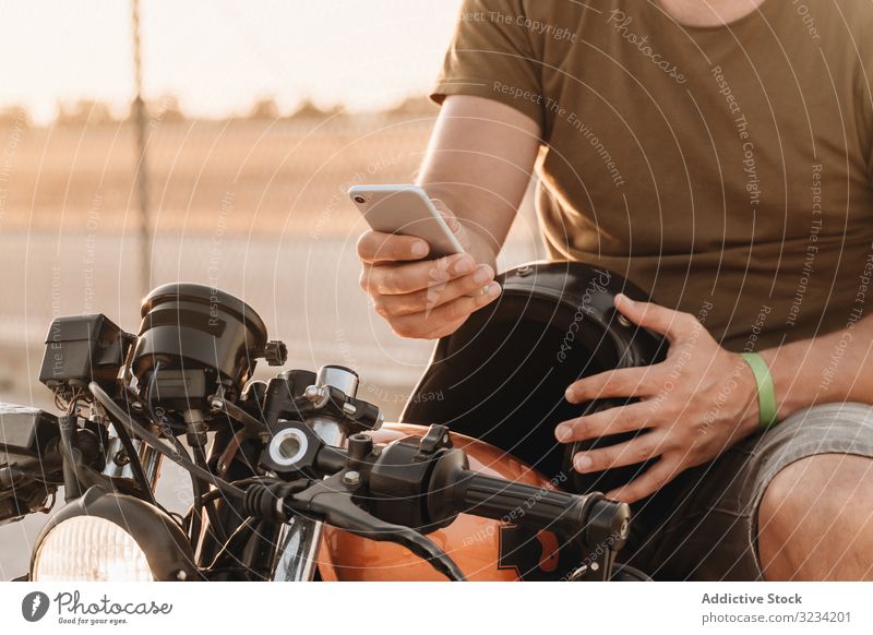 Mann sitzt auf Motorrad und surft mobil Smartphone moto ruhen benutzend Surfen Sonnenbrille fokussiert wehmütig sitzen Mobile männlich Feld Verkehr Straße
