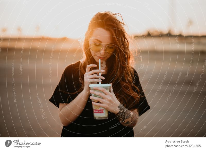 Langhaariges Teenager-Mädchen trinkt Milchshake Frau tausendjährig heiter cool Stil trinken Glück Sonnenuntergang Tattoo Sonnenbrille Piercing Freizeit Lächeln