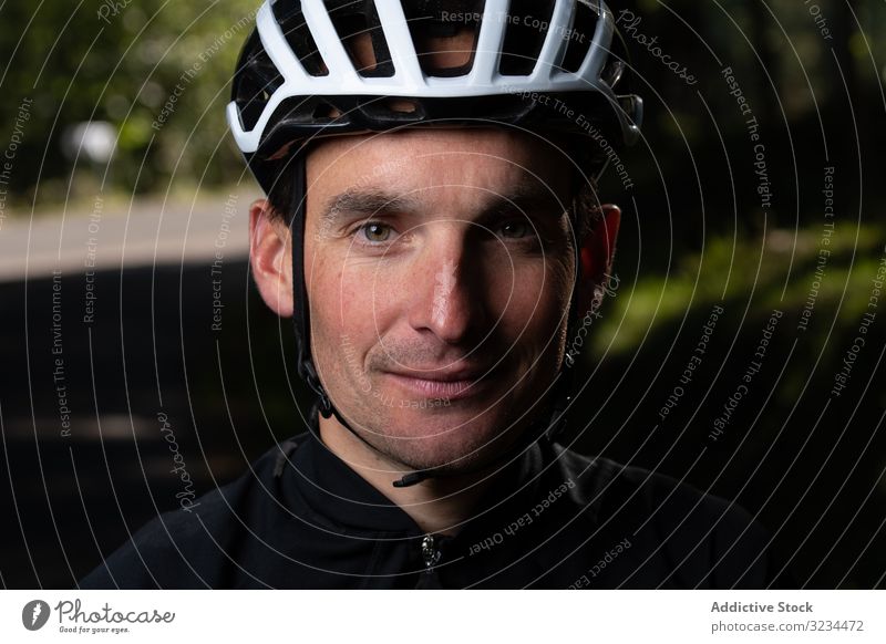 Positiver Radfahrer schaut auf Kamera im Park Training positiv Mann Lächeln Schutzhelm sonnig tagsüber Sport Sommer männlich Sicherheit froh zufrieden