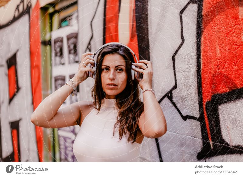 Frau, die Musik hört und ein Smartphone benutzt Kopfhörer hören Sommer Graffiti Beton Straße urban Streetstyle Grunge soziale Netzwerke Lächeln Glück Apparatur