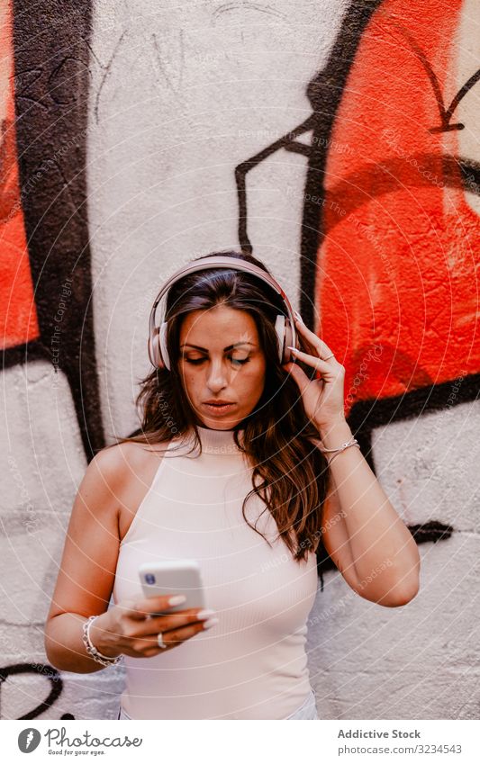 Frau, die Musik hört und ein Smartphone benutzt Kopfhörer hören Sommer Graffiti Beton Straße urban Streetstyle Grunge soziale Netzwerke Apparatur farbenfroh