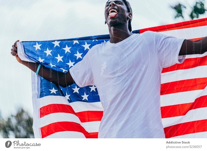 Schwarzer Mann wickelt sich draußen in amerikanische Flagge ein Amerikaner Fahne eingewickelt schwarz Afroamerikaner national Selbstständigkeit aktiv 4. Juli