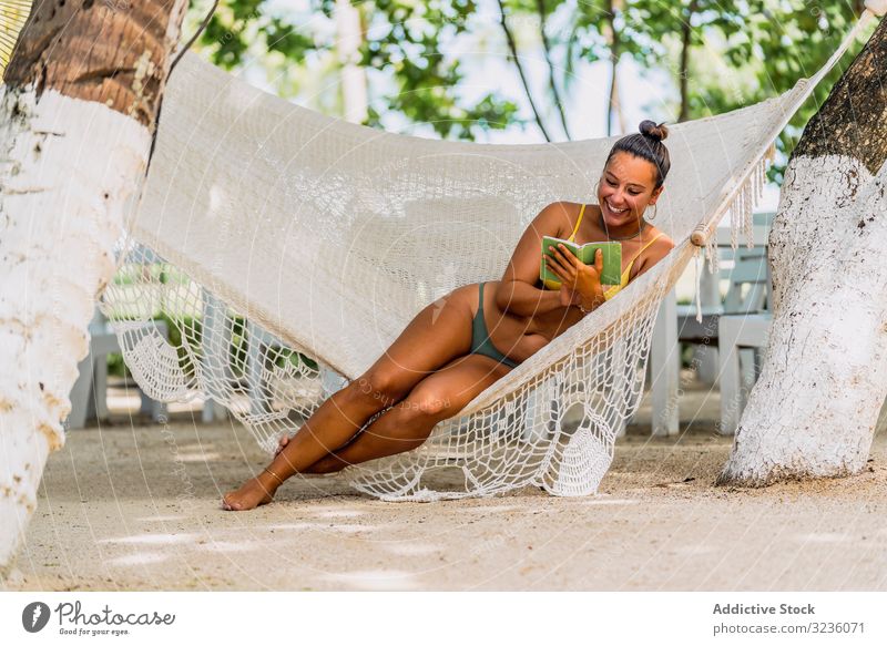 Fröhliche Frau im Bikini ruht sich in einer Hängematte am Strand aus Eishügel ruhen sitzen freudig Glück Lächeln exotisch Seeküste Bräune Barfuß entspannt jung
