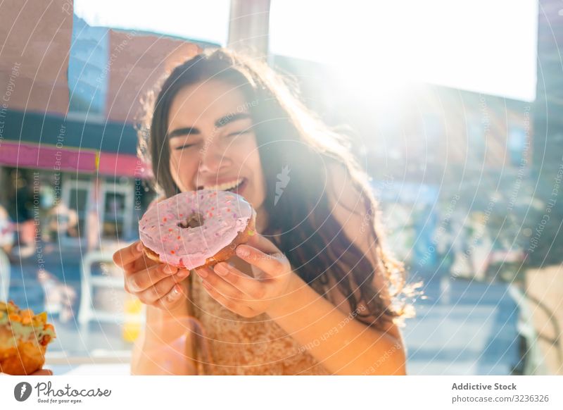 Frau genießt leckeren Donut im Cafe Krapfen Café essen genießen Biss Inhalt erfreut geschmackvoll Gebäck verglast rund Sonnenkleid sonnig Fenster Tisch sitzen