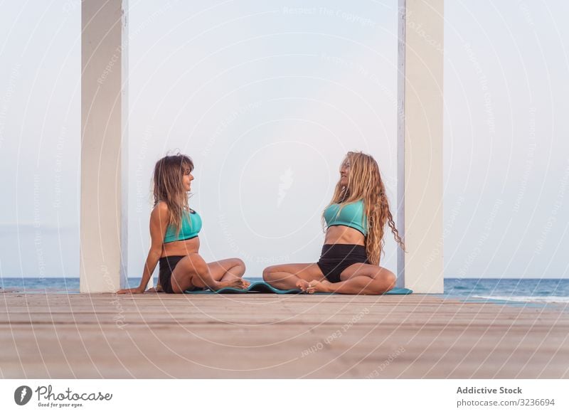 Lächelnde Frauen sitzen und strecken sich in Schmetterlingshaltung am Meer acroyoga Streckender Schmetterling Körperhaltung Übung Strand Seeküste Zusammensein