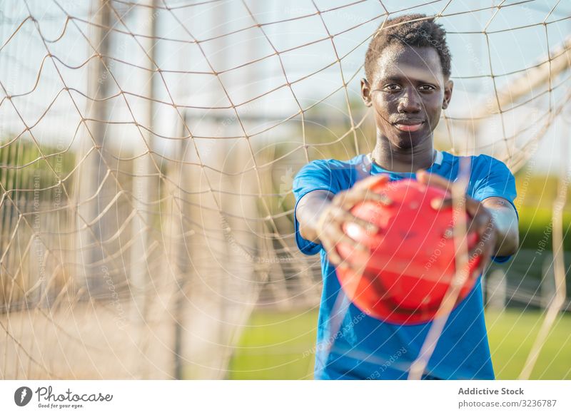 Afroamerikanischer Fußballspieler mit Ball Teenager ausgestreckte Arme Himmel wolkenlos Training Sportbekleidung ethnisch zeigen männlich Jugendlicher Rasen