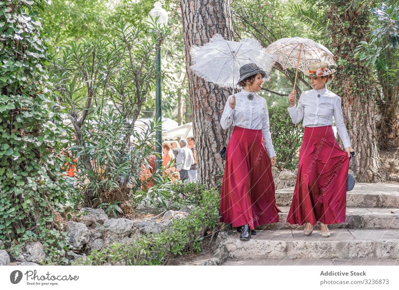 Vintage-Frauen gehen gemeinsam im Park spazieren Spaziergang reden altehrwürdig Schritt Kleid Sonnenschirm Lächeln Tracht Sommer Veranstaltung retro altmodisch