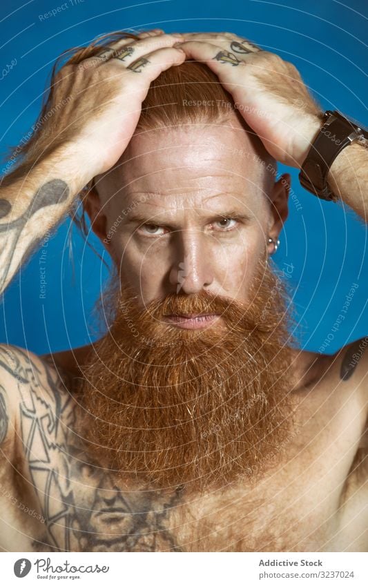 Selbstbewusster erwachsener rothaariger Hipster, der Haare berührt und in die Kamera schaut Mann rote Haare selbstbewusst Vollbart Schnurrbart nachdenklich