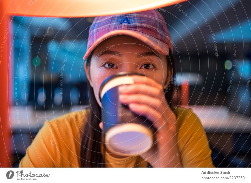 Asiatische Frau trinkt Kaffee am Tisch unter einer brennenden Lampe trinken Flughafen Einwegbecher Beteiligung Getränk asiatisch Imbissbude heiter Erholung