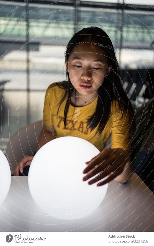 Asiatin untersucht runde Lampen auf dem Tisch Frau Licht kreativ Aufregung Saal beleuchtet Innenbereich asiatisch Kunst Design elektrisch Kraft Glühbirne