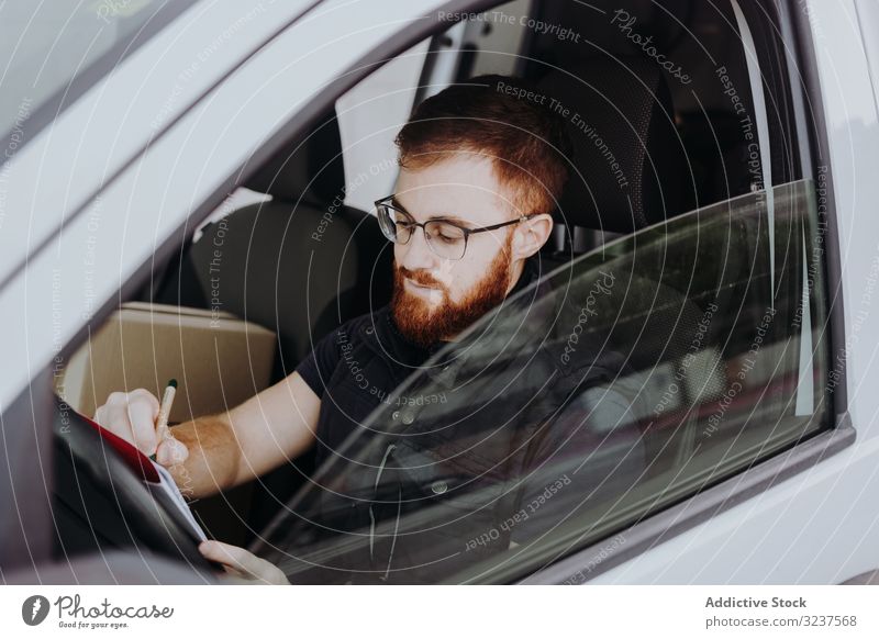 Kurier füllt Papiere aus, während er die Auslieferung der Bestellung an den Kunden im Auto vorbereitet PKW besetzen Versand achtsam Mann schreiben nachdenklich