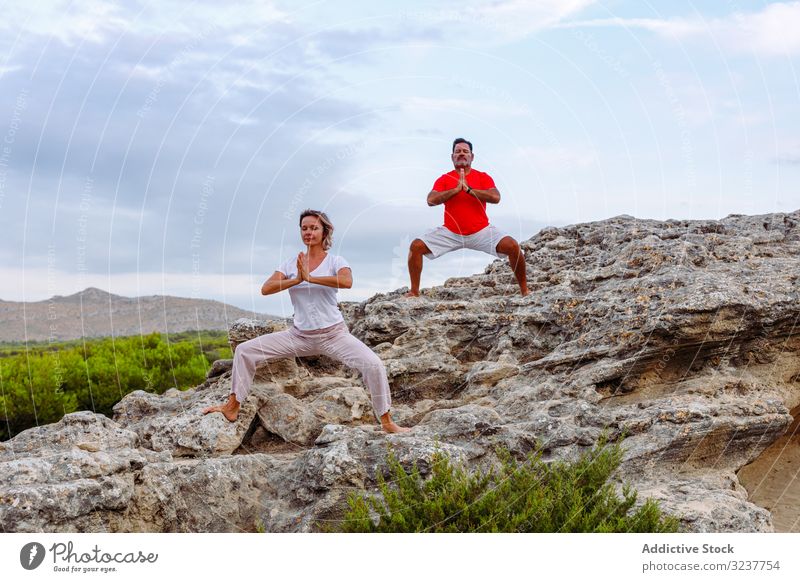 Paar meditiert auf Felsen Meditation Atem Übung Tai Chi umklammerte Hände geschlossene Augen Natur Himmel wolkig Training Frau Mann Erwachsener Gesundheit