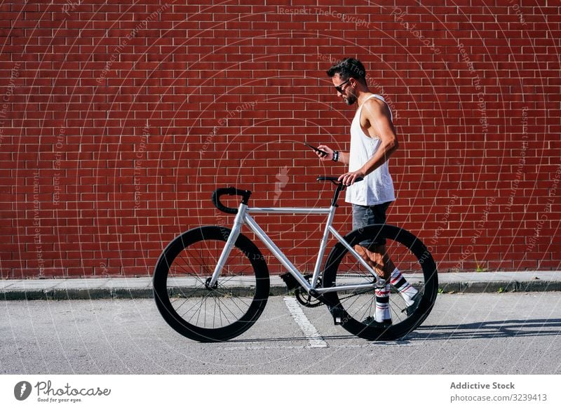 Sportlicher Mann mit Fahrrad beim Telefonieren stehen Handy benutzend modern sportlich aktiv Sommer männlich Sonnenbrille Radfahrer Smartphone Nachricht Texten