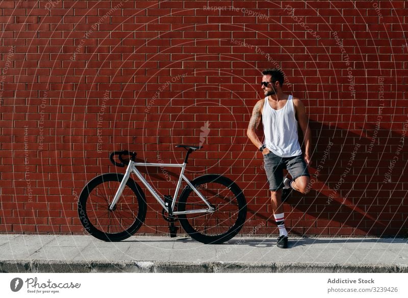 Sportlicher Mann mit Fahrrad an der Ziegelmauer stehend ruhen Backsteinwand modern sportlich aktiv Lehnen sich[Akk] entspannen Sommer männlich gutaussehend