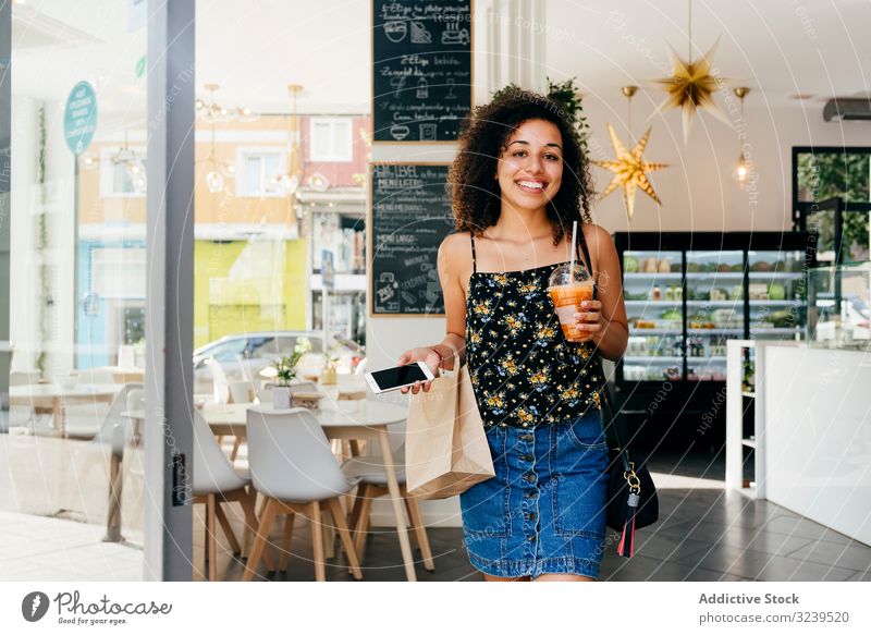 Fröhliche ethnische Frau verlässt Restaurant Café trinken Gesundheit Lächeln Smartphone Tüte lassen urban Vitamin Getränk Saft Smoothie Tasse Entzug heiter