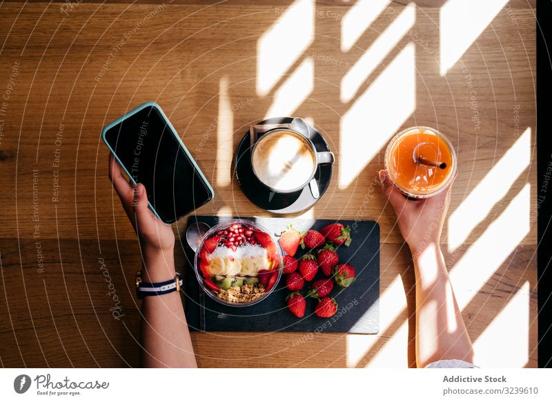 Frau frühstückt gesund und telefoniert Frühstück gesunde Ernährung Smartphone Tisch Erdbeeren Smoothie Schüssel Frucht Kaffee Lebensmittel hölzern Saft
