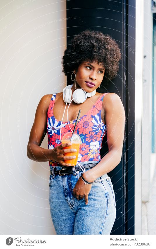 Charmante schwarze Frau mit einem Becher Saft Gesundheit trinken träumen farbenfroh Stil jung lässig Afroamerikaner Imbissbude Kopfhörer nachdenklich Tasse