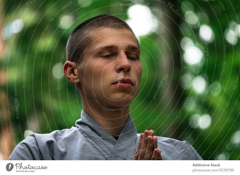 Junger Mann meditiert im Garten kämpferisch Training Meditation umklammerte Hände taiji rückzug Übung Uniform üben männlich kahl fokussiert ernst konzentriert