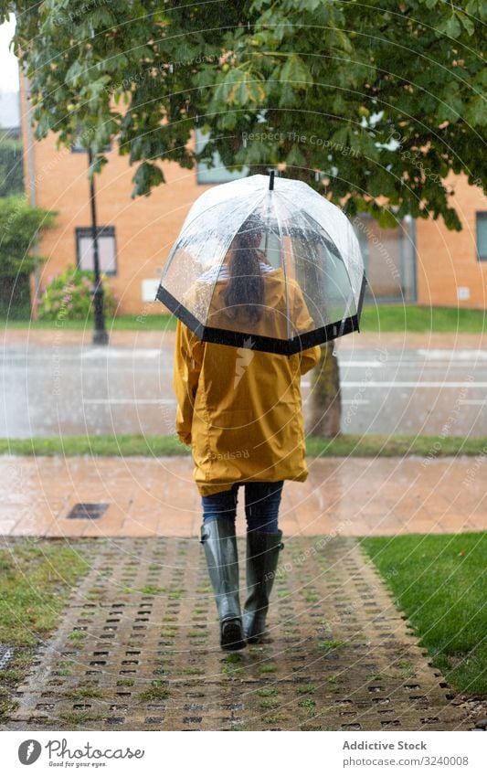 Frau in gelbem Regenmantel und Gummistiefeln mit Regenschirm bei Regen Straße nass Pfütze Herbst laufen Saison Wetter Umwelt Stiefel Oktober Schutz traditionell