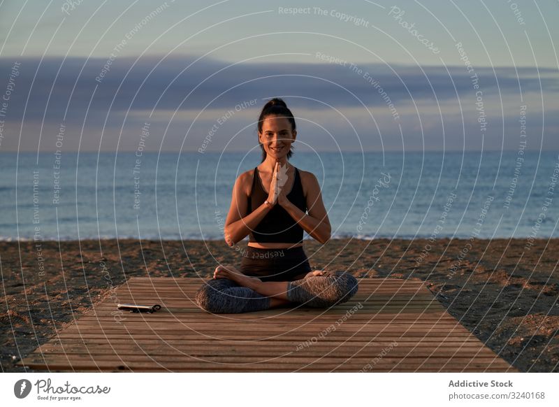 Erwachsene Frau meditiert abends am Meer Yoga MEER Strand Asana Aktivität Abend passen umklammerte Hände gekreuzte Beine Himmel wolkig positiv Lächeln schlank