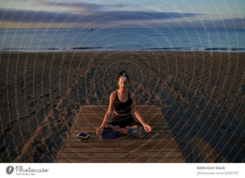 Barfüssige Frau meditiert auf Holzpfad Yoga Strand Asana Aktivität Lotus-Pose passen geschlossene Augen gekreuzte Beine Weg schlank Sportbekleidung Training