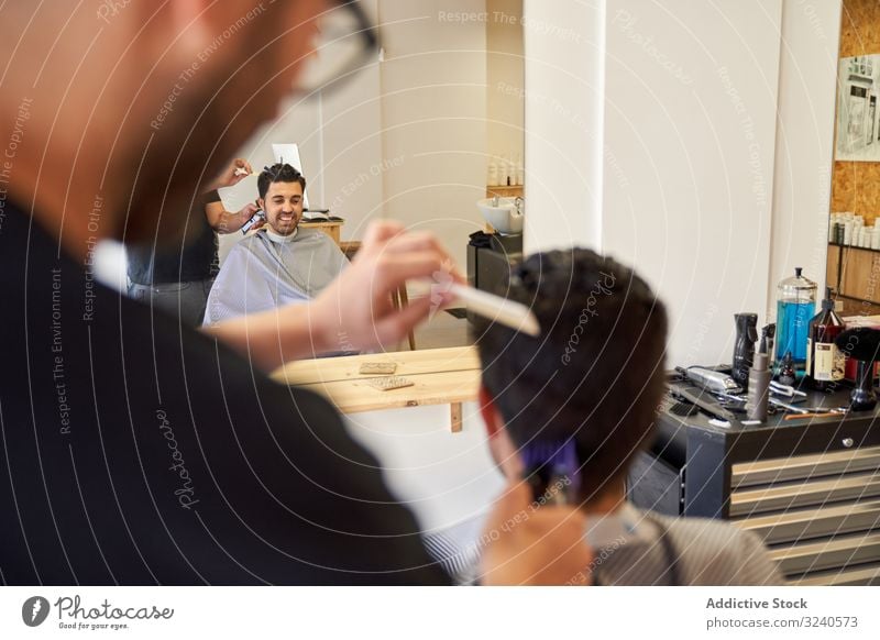 Reflexion im Spiegel eines Friseurs, der mit einer Maschine Haare schneidet, an einen Kunden, der auf dem Friseurstuhl sitzt Rasierapparat geschnitten