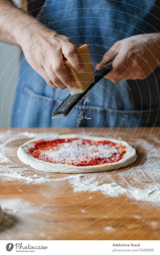 Pflanzenkoch, der Käse auf Pizza mahlt Mann Teigwaren Grinden Saucen Mehl weich frisch Küche Vorbereitung Lebensmittel Küchenchef Italienisch männlich Schürze