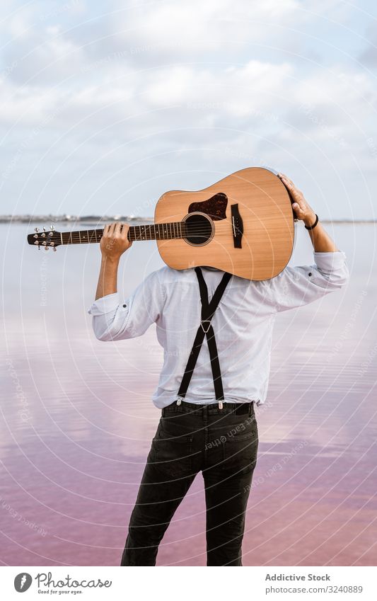 Musiker, der am Strand steht und die Gitarre hinter dem Rücken trägt führen Starrer Blick Mann akustisch neu modern USA stehen Halt Ufer jung Erwachsener