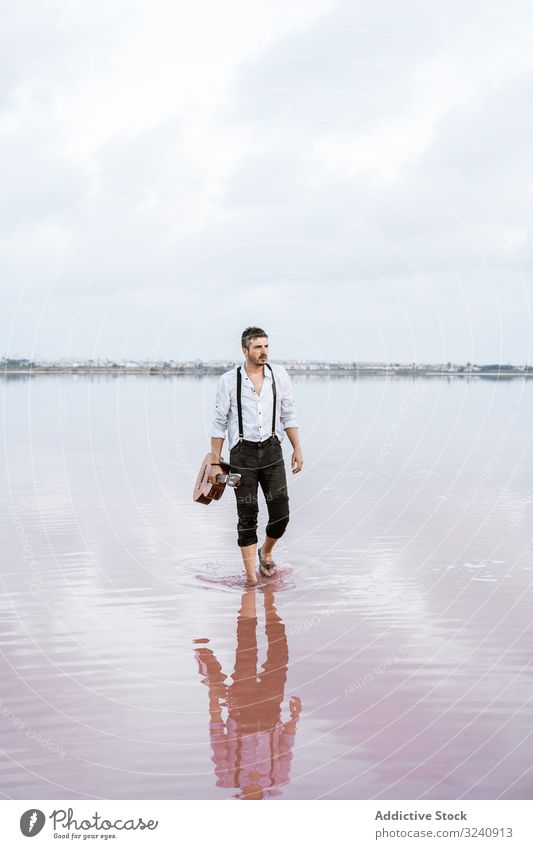 Musiker mit Gitarre am Meer inspiriert Seeküste Barfuß stehen Beteiligung spielen Wasser wolkig Mann Ufer weißes Hemd Hosenträger Horizont