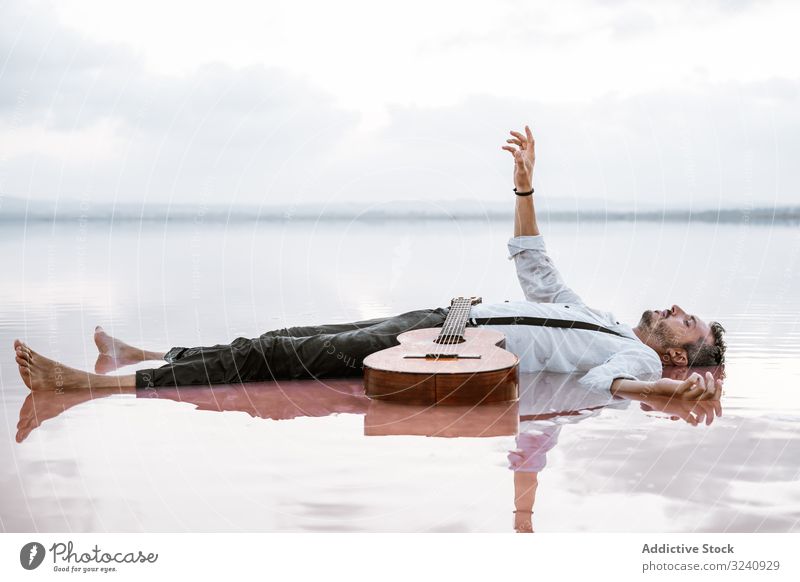 Im Wasser liegender Mann mit Gitarre am Meer ruhen Seeküste stilvoll auf dem Rücken liegend fliegend MEER Sandbank weißes Hemd Hosenträger verträumt friedlich